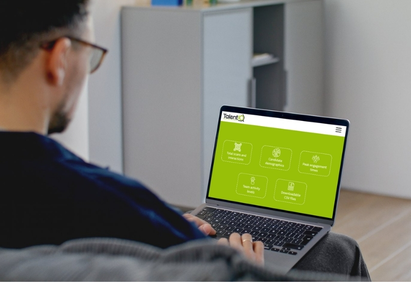 A person sitting on a sofa, viewing a laptop displaying the TalentIQ website, which features a green background and various navigation buttons.